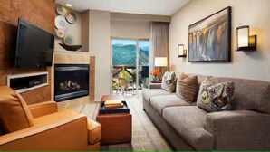 A modern living room with a fireplace, a sofa, a television, and a balcony with a mountain view.