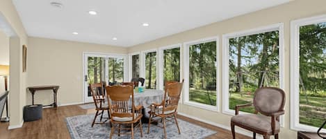 A dining area with a table and chairs, large windows, and a view of the outdoors.