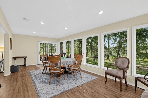 A dining area with a table and chairs, large windows, and a view of the outdoors.