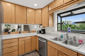 A modern kitchen with wooden cabinets, a dishwasher, a sink with a faucet, and a window with a view of greenery.