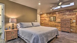 Quarto com uma cama, mesa de cabeceira, luminária, parede de madeira, ventilador de teto e guarda-roupa.