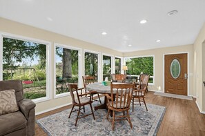 A dining area with a table and chairs, large windows, and a door.