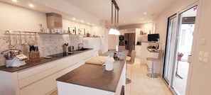 Uma cozinha moderna com ilha central, área de jantar com mesa e cadeiras, e uma TV fixada na parede.