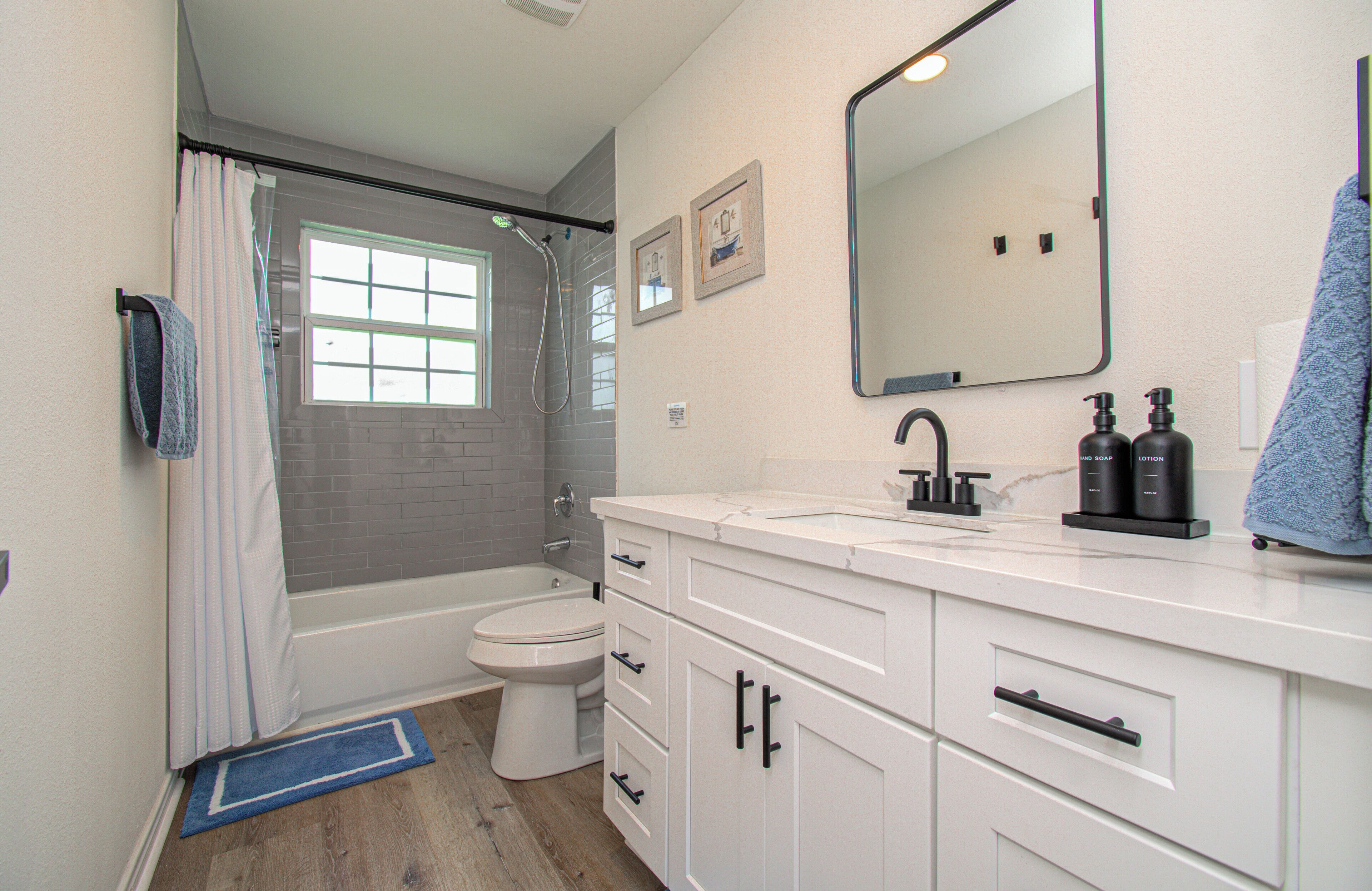 A bathroom with a shower, toilet, sink, and mirror.