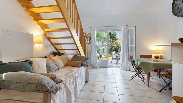A bedroom with a wooden staircase, a bed with pillows, a dining table with chairs, and a view through a glass door. - La Maisonnette du Soleil (La Tranche-sur-Mer)