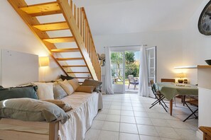 A bedroom with a wooden staircase, a bed with pillows, a dining table with chairs, and a view through a glass door. - La Maisonnette du Soleil (La Tranche-sur-Mer)