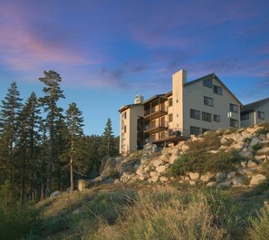 A multi-story building with a modern architectural design, situated on a rocky hillside with a forest backdrop.