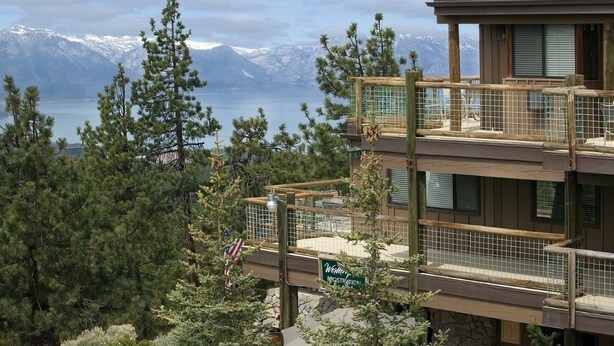 Un edificio de varios pisos con vistas a montañas nevadas y un lago.