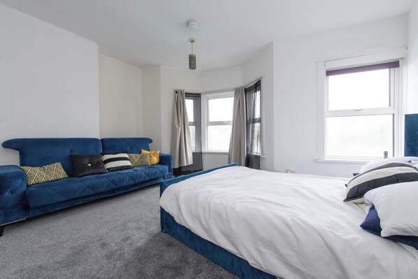 A bedroom with a bed, a blue sofa, and a window.