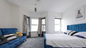 Un dormitorio con un sofá azul, una cama con ropa de cama blanca y una ventana con cortinas.