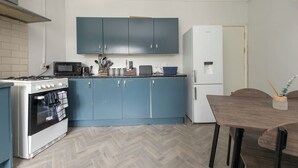 Cocina compacta con estufa, microondas y refrigerador. Cuenta con una mesa de comedor con sillas y un mueble azul sobre la encimera.