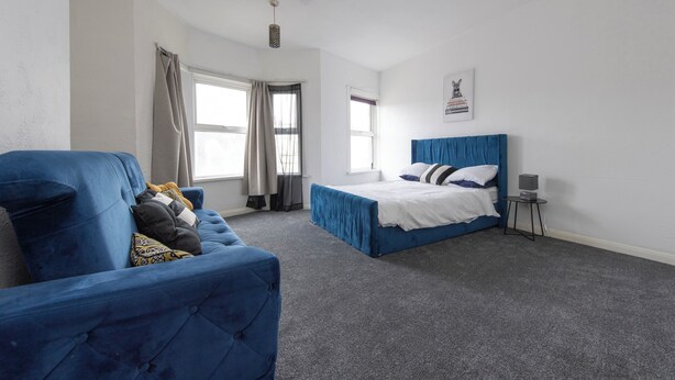 Un dormitorio con una cama azul, un sillón azul y una mesita de noche con una lámpara.