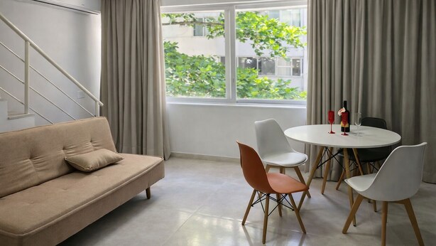 A modern living room with a beige sofa, a dining table with four chairs, and a view of greenery outside. - Apartment just minutes from Copacabana Beach. (Rio de Janeiro)