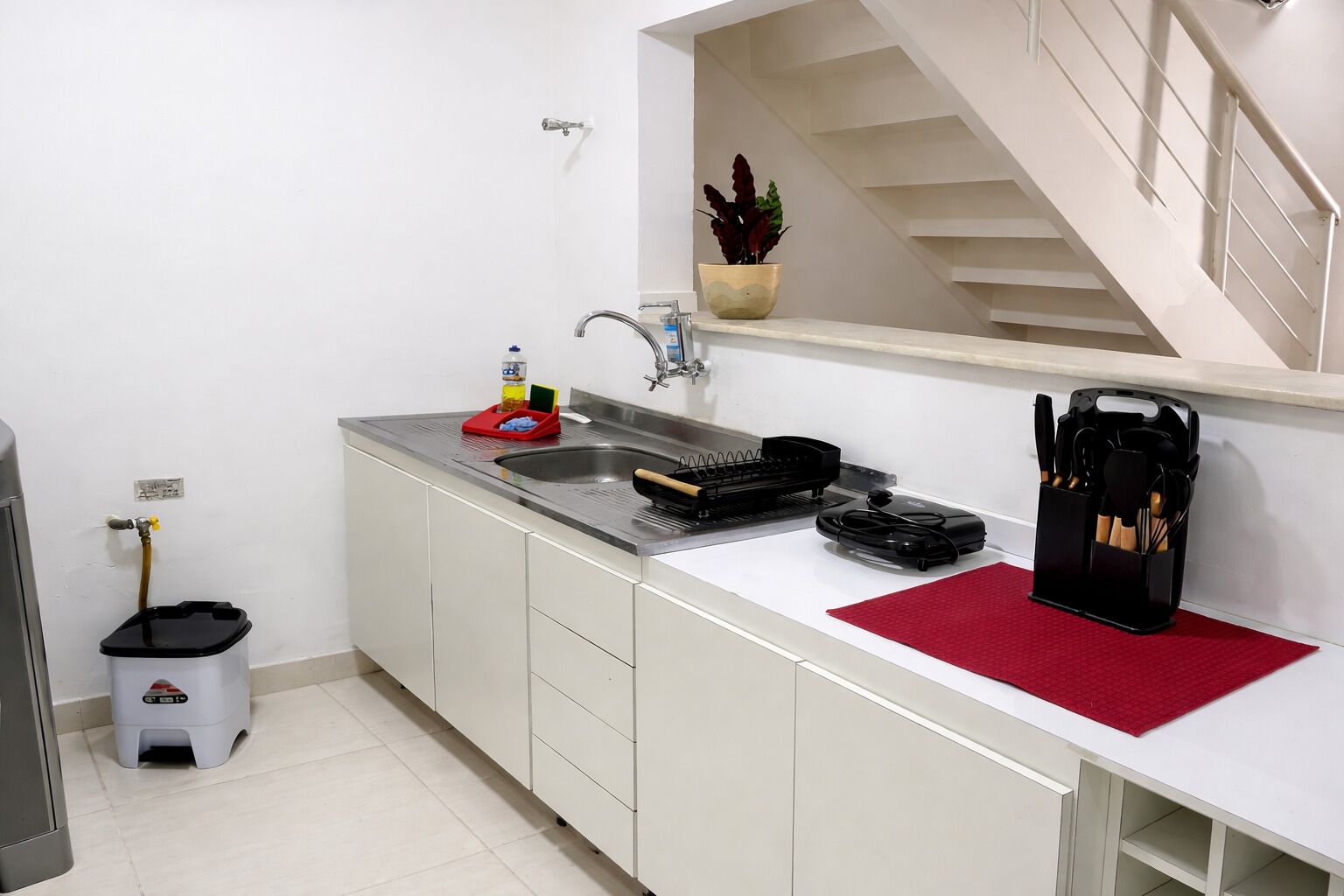 Une petite cuisine équipée d’un évier, d’une petite poubelle, d’un robinet et d’une plante en pot posée sur le plan de travail.