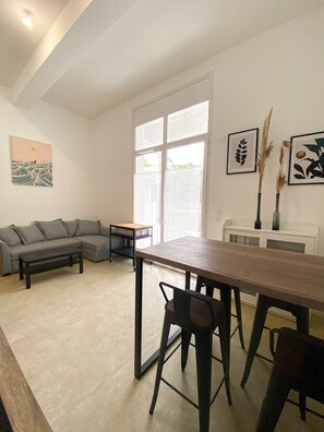 Un salon comprenant un canapé, une table basse, une table à manger avec des chaises et des œuvres d’art accrochées aux murs.