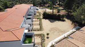 Ein Hotel mit terrakottafarbenen Dächern, einem Sandhof und einer bewaldeten Umgebung im Hintergrund.