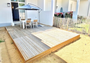 Une terrasse en bois avec une table et des chaises, un parasol et une clôture blanche.