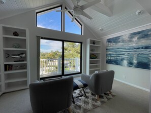 Ein modernes Wohnzimmer mit großem Fenster, Deckenventilator und Blick ins Freie.