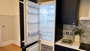 Ett kompakt kök med ett inbyggt kylskåp, en liten arbetsbänk och en kakelbeklädd vägg bakom.
