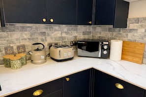 Une cuisine avec des meubles de couleur sombre, un four à micro-ondes, un grille-pain, une bouilloire et une planche à découper en bois.