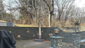 A stone wall with a metal lamp post and a covered grill in a park setting.