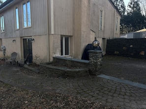 A two-story house with a stone staircase leading to the front door, a covered grill area, and a paved driveway.