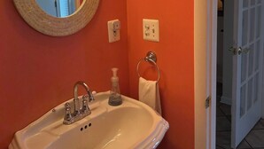 A bathroom with a white sink, a round mirror, and a wall-mounted light fixture.