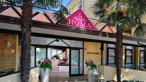 A hotel entrance with a prominent sign, a reception desk, and outdoor seating. - Albergo Roma (Gatteo a Mare)