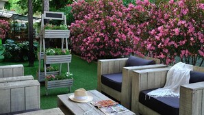 A wooden outdoor seating area with cushions, a hat, and a magazine on a table. - Albergo Roma (Gatteo a Mare)