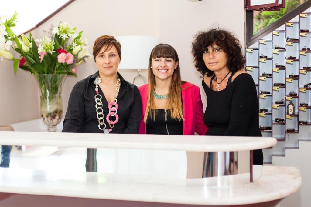 Three individuals standing in a modern interior space with a marble counter and a wall displaying multiple framed items.
