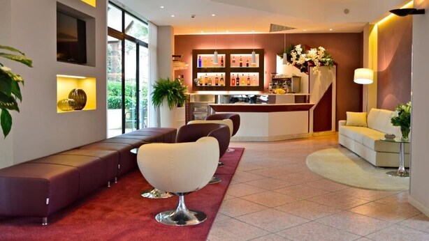 A modern hotel lobby with a reception desk, seating area, and a bar. - Albergo Roma (Gatteo a Mare)