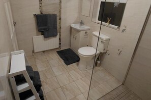 A small bathroom with a toilet, sink, and a mirror. There is a towel hanging on the radiator and a small window with a view of the sky.