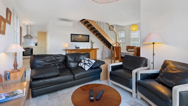 Una sala de estar moderna con un sofá, un sillón, una mesa de centro y controles remotos.