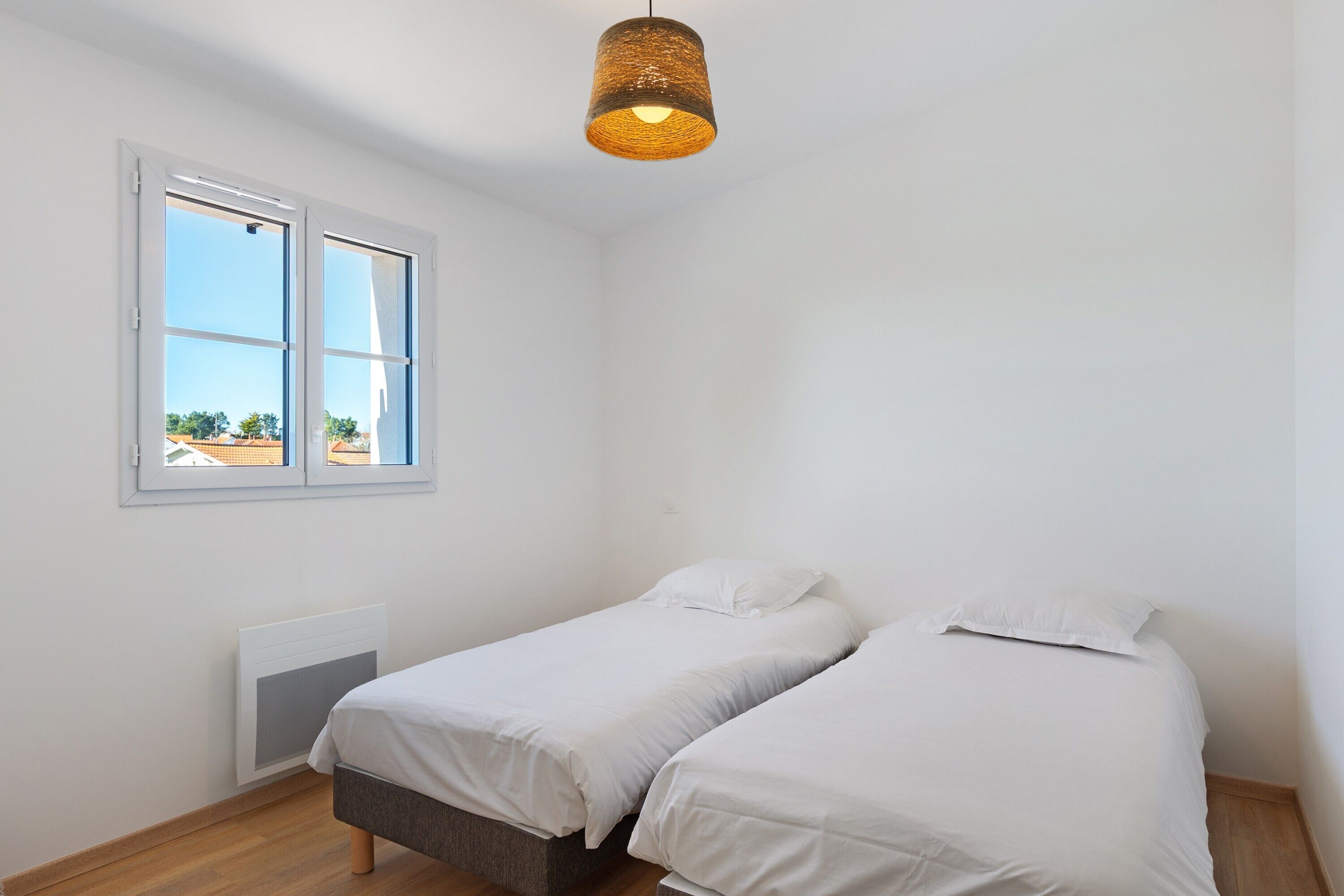 A room with two beds, a window, a radiator, and a hanging light fixture.