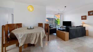 Una sala de estar moderna con comedor, sofá, televisor y un amplio ventanal.