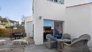 Un patio con mobiliario de mimbre, una terraza de madera y un ventanal corredizo que da a un espacio interior.