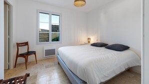 Un dormitorio con cama, una silla, un ventanal y una lámpara colgante.