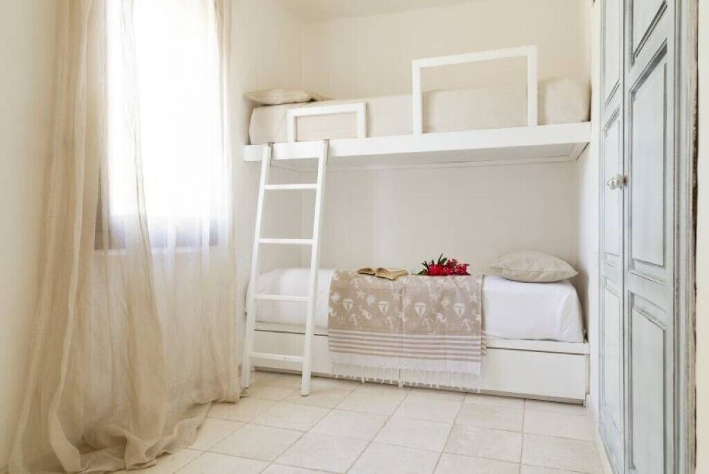 Een slaapkamer met stapelbed, een ladder, een raam met dunne gordijnen en een witte kast.