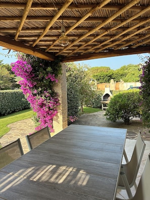 Eine Terrassengruppe im Freien mit einem Holztisch und Stühlen, umgeben von üppigem Grün und bunten Blumen.