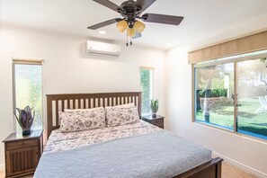 Ein Schlafzimmer mit Bett, Deckenventilator, Klimaanlage, Fenster und Nachttisch mit Pflanze.