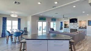 A modern kitchen with a large island, wooden flooring, and a dining area with blue chairs.