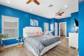 Une chambre à coucher avec un lit, des ventilateurs de plafond, une table de chevet et une commode.