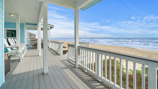 A wooden deck with white railings overlooking a beach.
