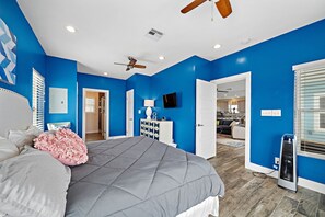 Une chambre avec un grand lit, un ventilateur de plafond, une commode et un téléviseur.