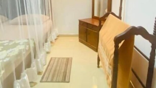 Ein Schlafzimmer mit einem Moskitonetz über dem Bett, einem Holzschrank, einem Spiegel und einem Nachttisch.