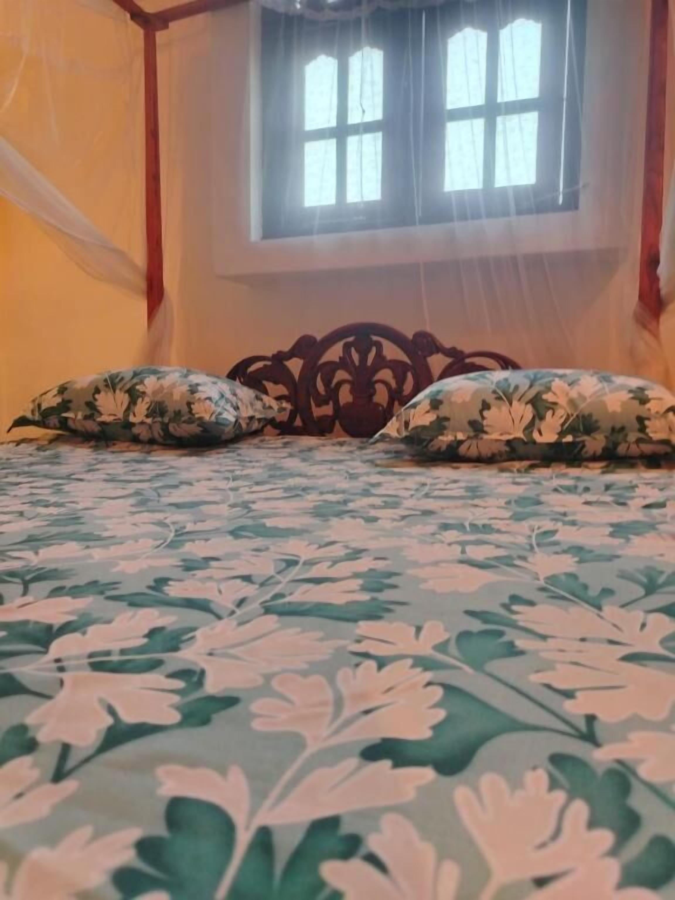 A bed with floral bedding and a wooden headboard, a window with curtains, and a room with a simple layout.