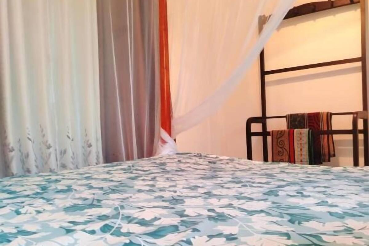 A bedroom with a bed covered in a floral-patterned bedspread, a wooden headboard, and a white canopy.