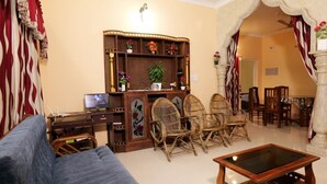 Ein Wohnzimmer mit einer Couch, einem Couchtisch, Korbstühlen, einer Holz-Multimediakommode mit Fernseher sowie einem Essbereich mit Stühlen und Tisch.