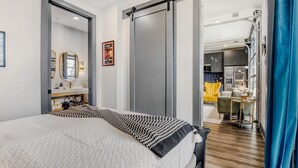 A modern bedroom with a large bed, a mirror, and a sliding door leading to a kitchen area. - Downtown Condo · Walk to Broadway · Free Parking (Nashville)