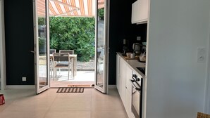 Una cocina moderna con comedor, un ventanal corredero que da a un patio, y una pequeña zona de estar al aire libre.